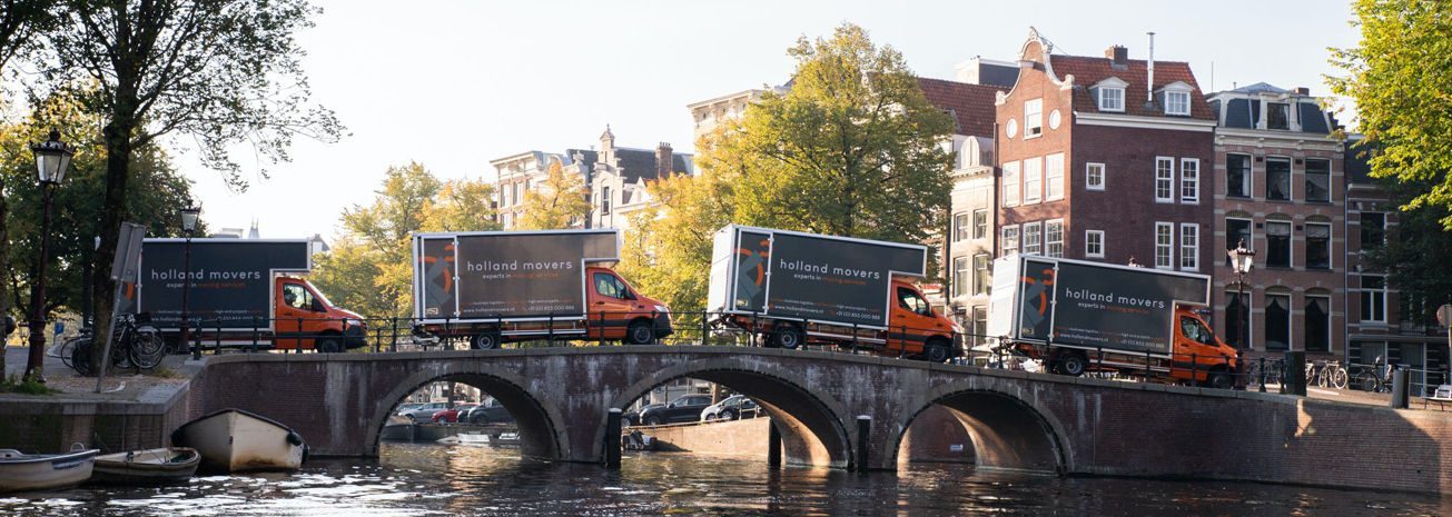 Vier verhuiswagens van het Amsterdamse verhuisbedrijf Holland Movers rijden over de grachten van Amsterdam